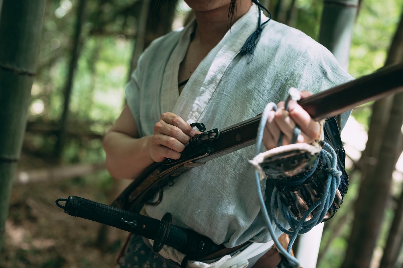 竹林で火縄銃に着火準備をする薄緑の半着姿の野盗［モデル：まーこ］