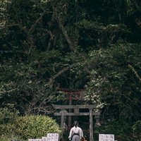 鳥居へと続く奉納石柱の参道を歩く袴姿の侍の後ろ姿の写真