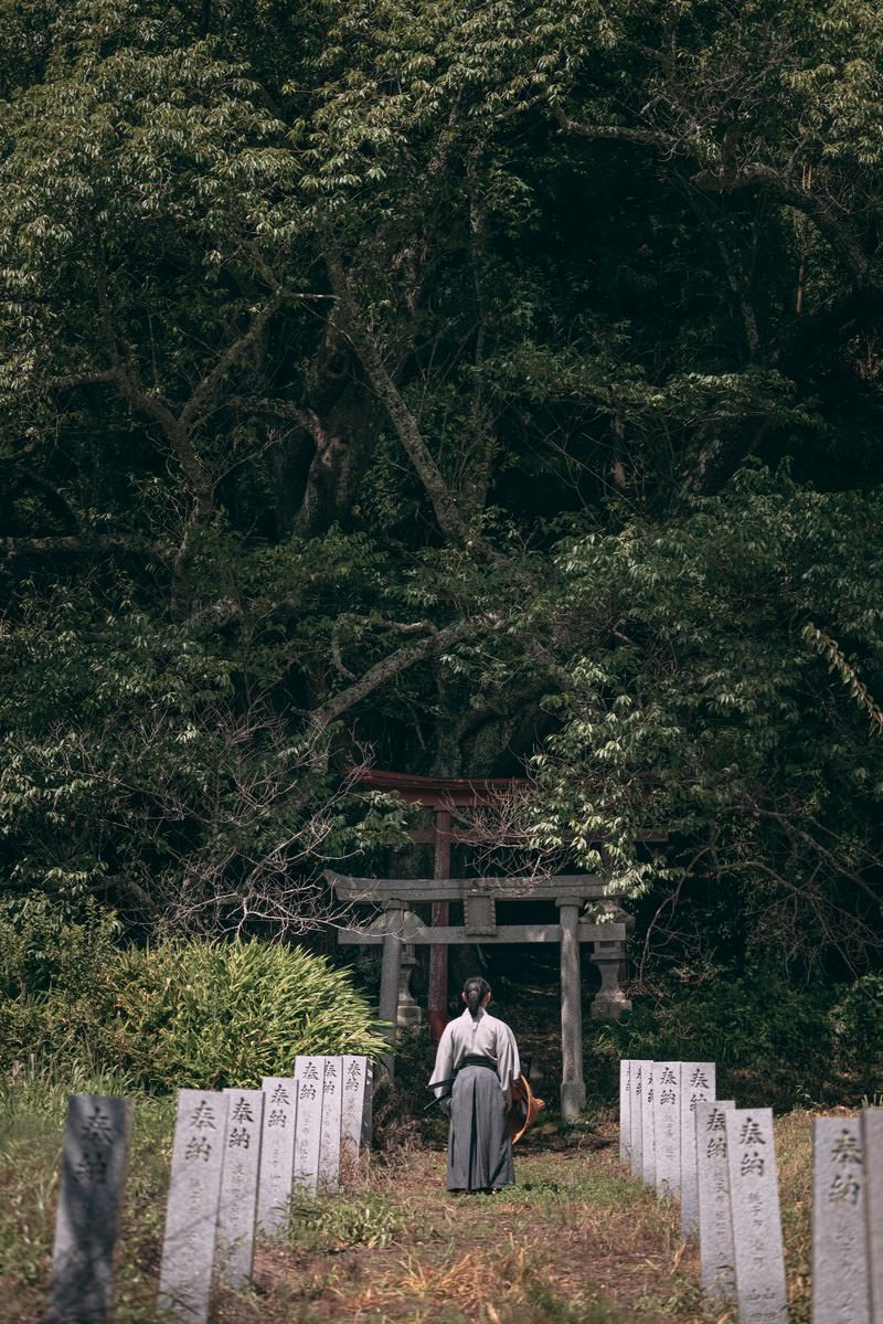 鳥居へと続く奉納石柱の石段を袴姿の武士が歩く後ろ姿［モデル：まーこ］