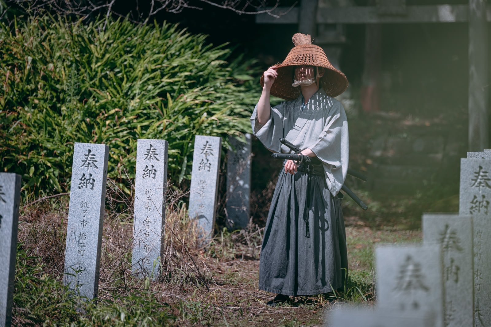 網代笠をかぶり袴を着た男性が神社の境内に立つ様子［モデル：まーこ］
