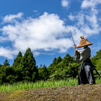 青空の下で刀を構える網代笠姿の武士の凛々しい姿の写真