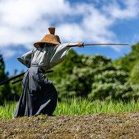 黒い袴と網代笠の侍が日本刀を抜刀する瞬間の写真