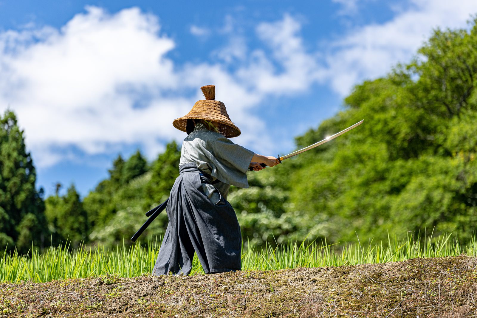 網代笠を被り袴を着た侍が日本刀を構えている様子［モデル：まーこ］