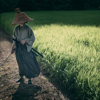 田んぼの脇で日本刀を抜いて構える笠を被った侍の写真