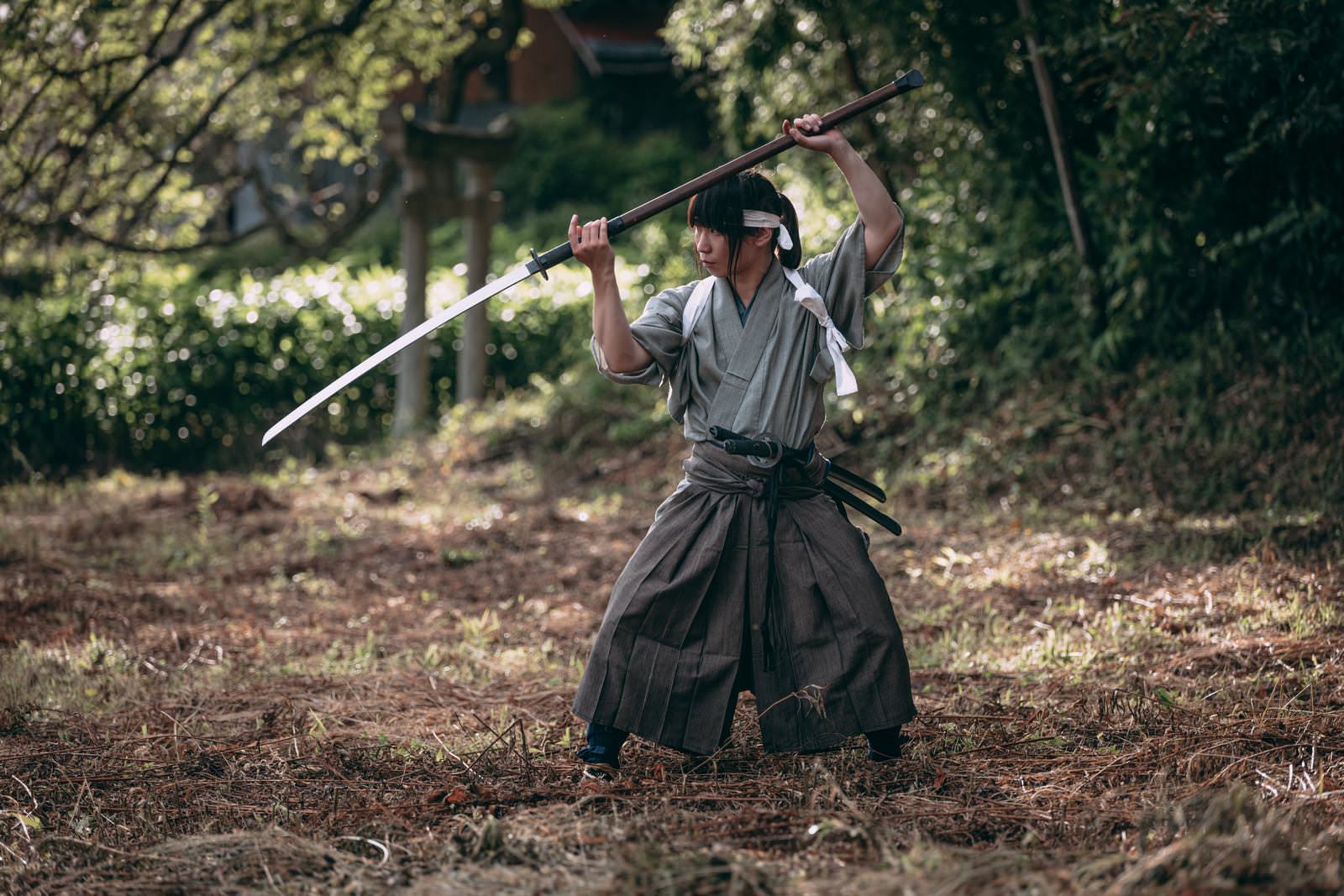 屋外で長巻を頭上に構える袴姿の侍［モデル：まーこ］