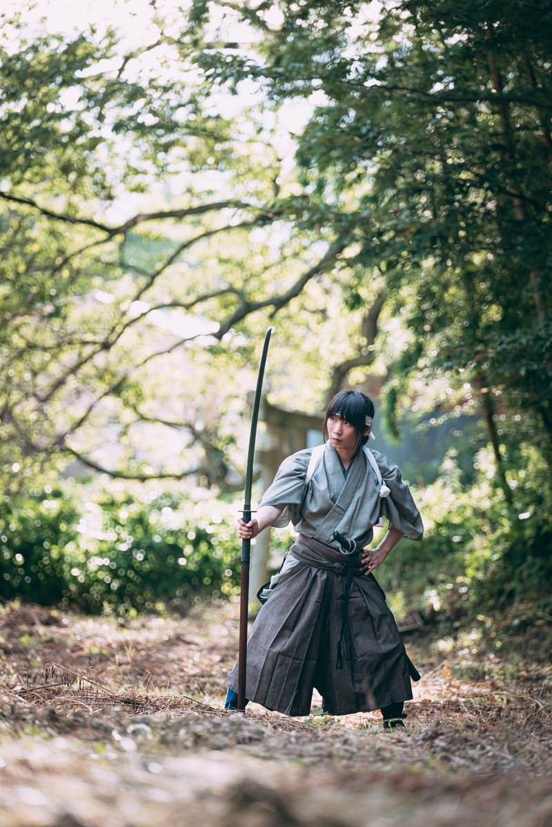緑の自然の中で長巻を構える白い袴姿の男性［モデル：まーこ］
