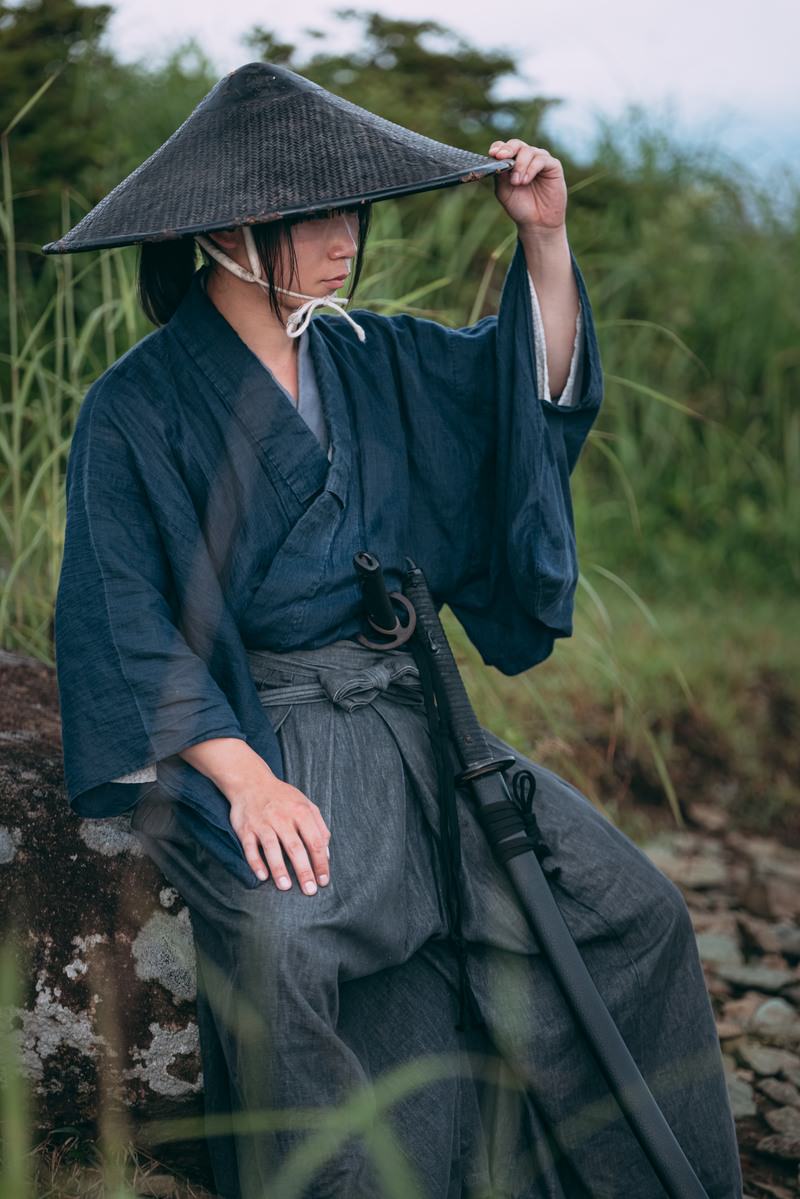 袴を着て網代笠を被った侍が岩の上に腰かけて休憩している［モデル：まーこ］