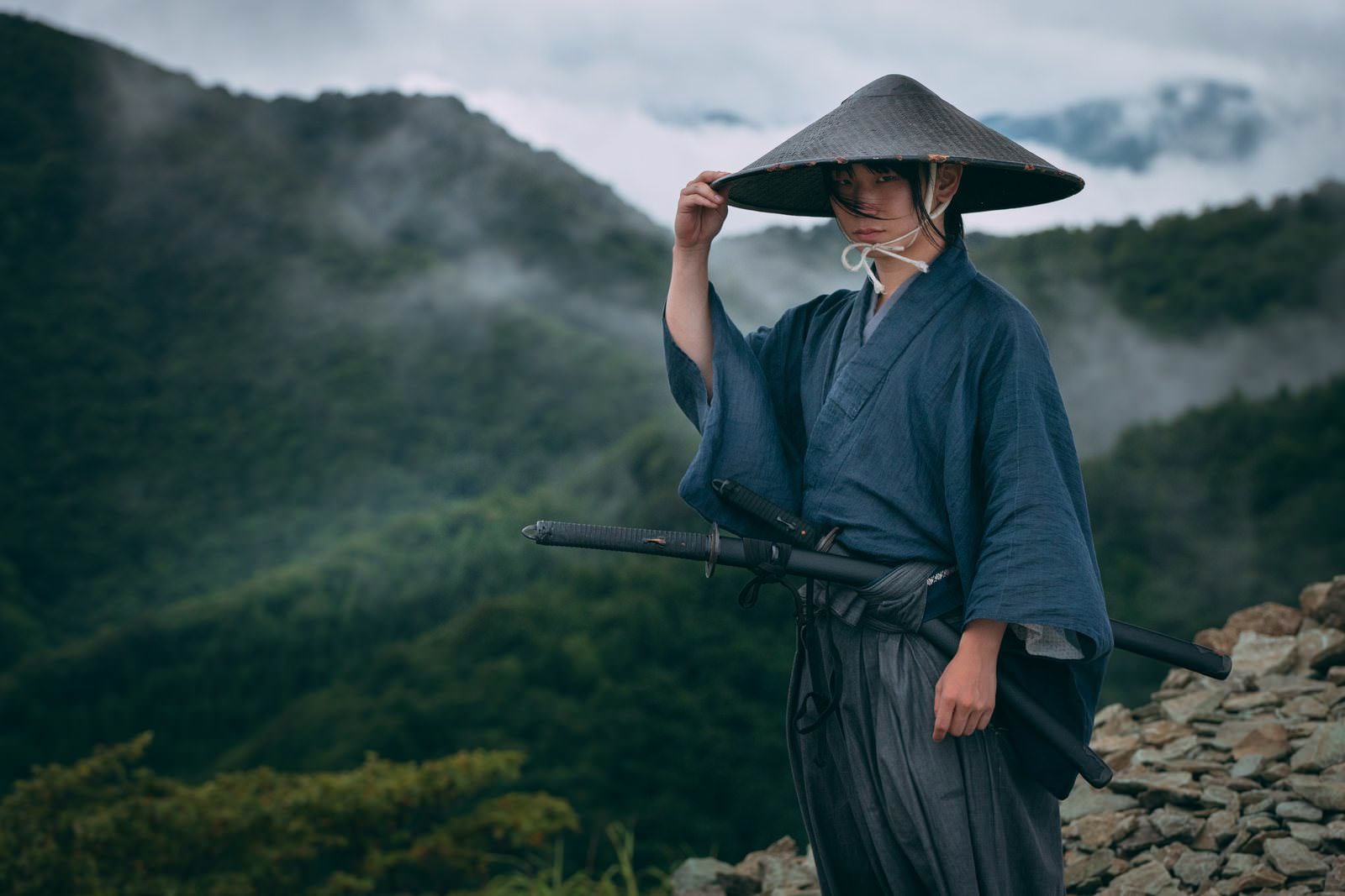 霧の山間で網代笠に右手を添える袴姿の侍の男性［モデル：まーこ］