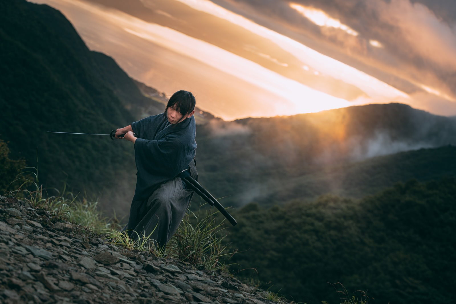 夕焼けの山で刀を構える侍［モデル：まーこ］