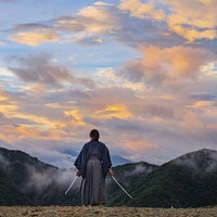 夕日に染まった空を背に二刀流を構える侍の後ろ姿の写真