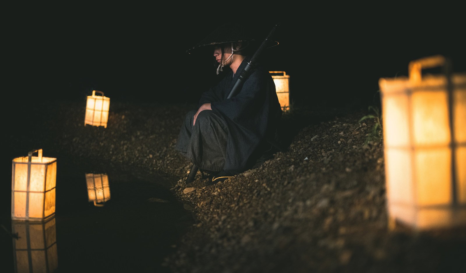 夜の屋外で行灯に囲まれて座る袴姿の侍［モデル：まーこ］