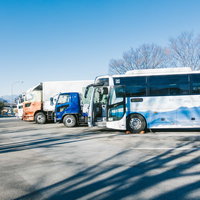 高速道路のパーキングエリアに停車中の高速バスと大型トラックの写真