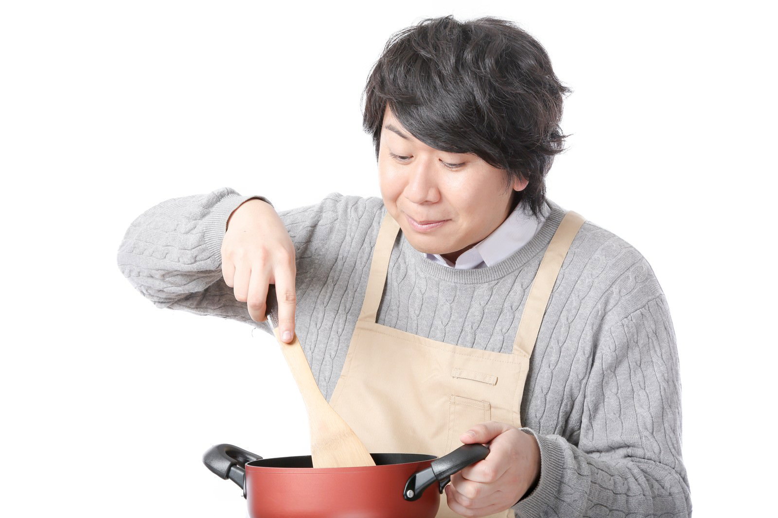 ベージュのエプロンを着けた男性が赤い鍋のスープをかき混ぜている［モデル：あまのじゃく］