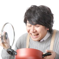 我慢できずに鍋の蓋をあけるエプロン姿の男性の写真