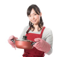 赤いエプロン姿で鍋を持ち微笑む新妻の料理風景の写真