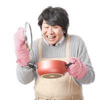 赤い鍋を持って笑顔がこぼれるエプロン男子の写真