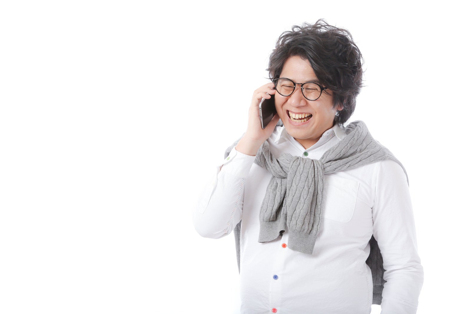 白いシャツとグレーのストール姿の眼鏡をかけた男性が、スマートフォンで通話しながら笑顔で話している［モデル：あまのじゃく］