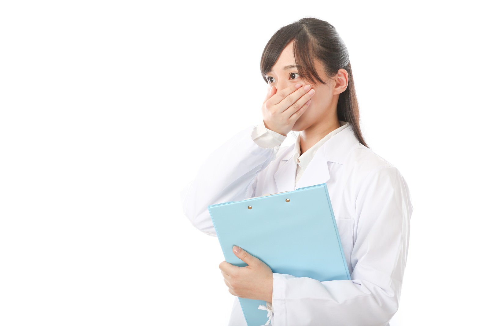 白衣を着た研修医の女性がクリップボードを持ち、口を抑えて驚いている［モデル：さとうゆい］