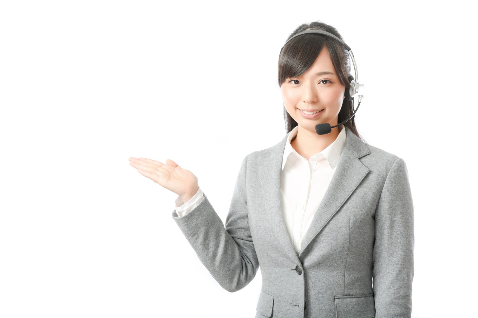 ヘッドセットを装着し、グレーのジャケット姿で左手を広げて笑顔で対応する女性オペレーター［モデル：さとうゆい］