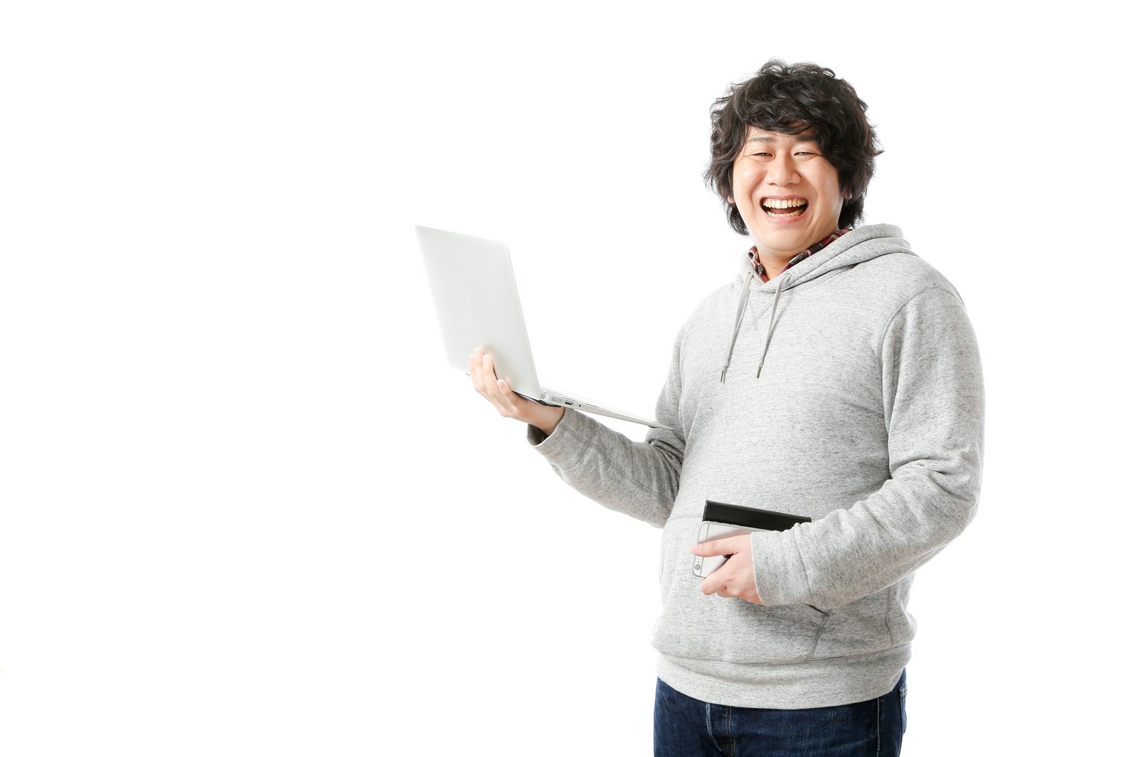 ノートパソコンを持って笑顔で振り返る男性。グレーのパーカー姿で仕事の充実感を表現［モデル：あまのじゃく］