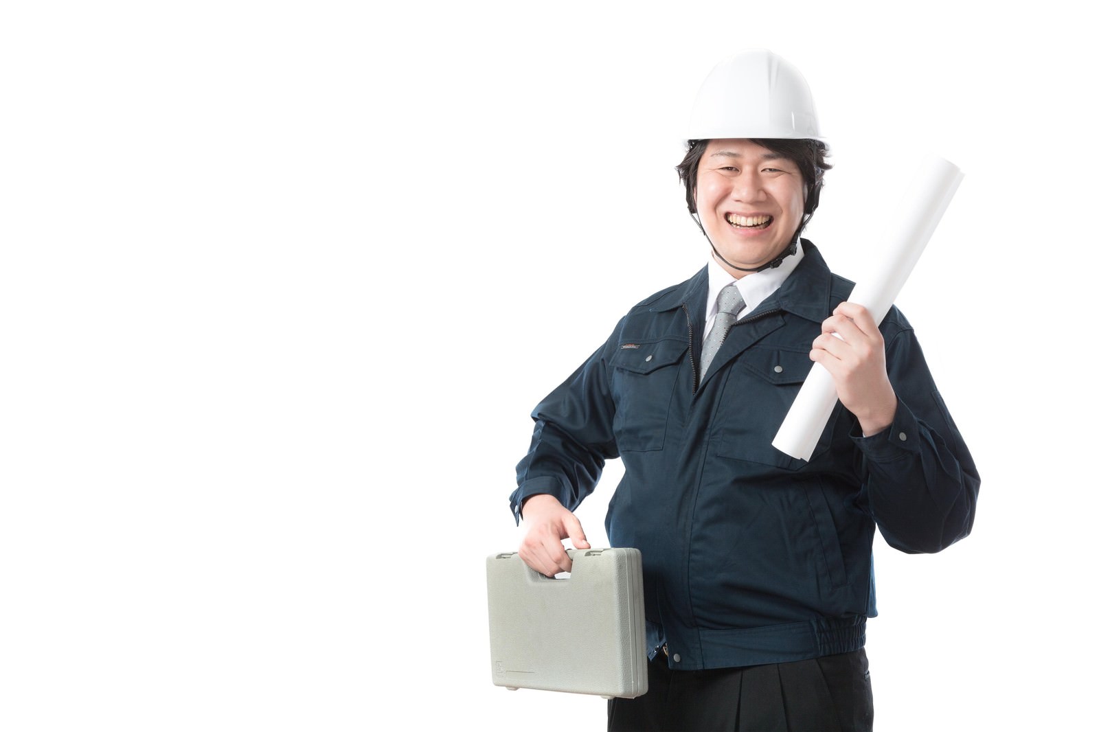 ヘルメット姿の作業着を着た男性が図面と工具箱を持ち笑顔で立つ［モデル：あまのじゃく］