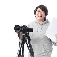 制作の現場で笑顔で絵コンテを手に映像機材を操作する男性ディレクターの写真