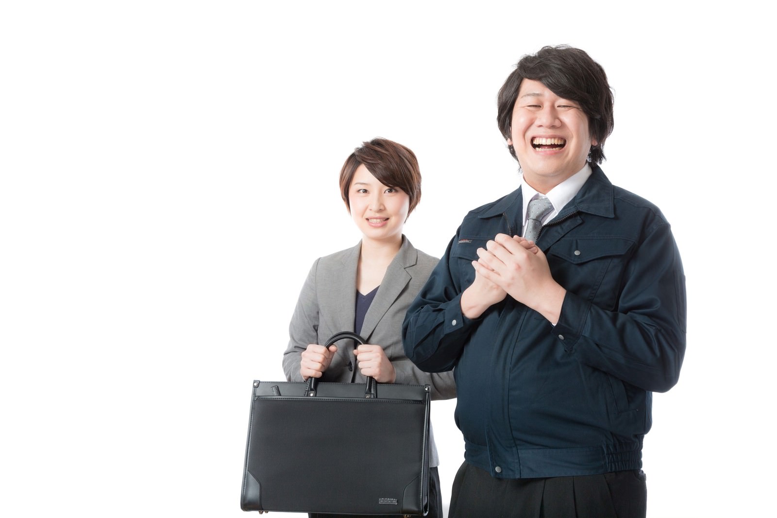 グレースーツの女性営業職がブリーフケースを持ち、紺ジャケットの男性営業職が両手を合わせて笑顔で対応している。［モデル：八木彩香 あまのじゃく］