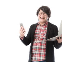 スマートフォンとノートパソコンを持つWebデザイナーの歓喜の写真