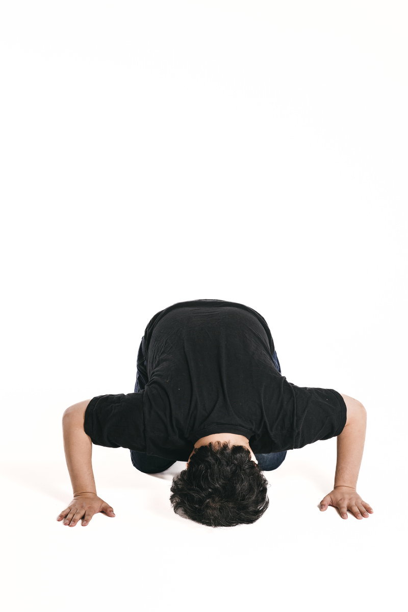 白い背景で土下座して頭を下げている黒いシャツの男性［モデル：段田隼人］