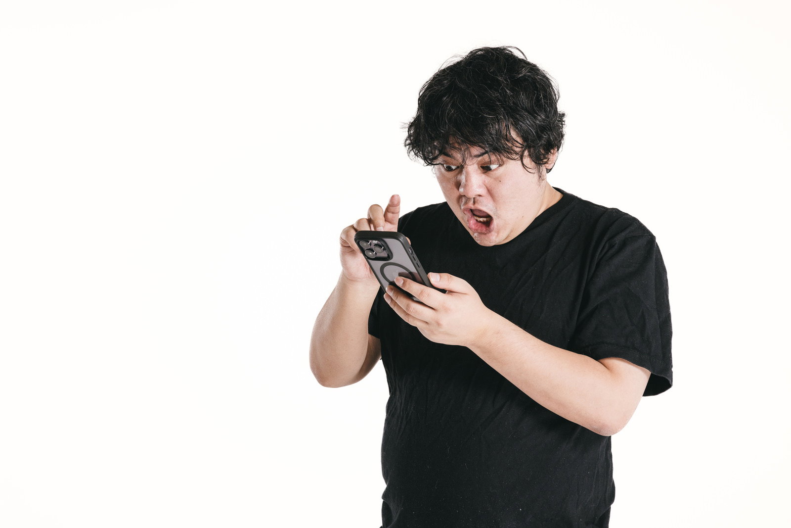 スマホを持って驚いた表情の男性［モデル：段田隼人］