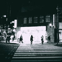 夜間の信号待ち、街頭灯に照らされた横断歩道で立つ人々の写真