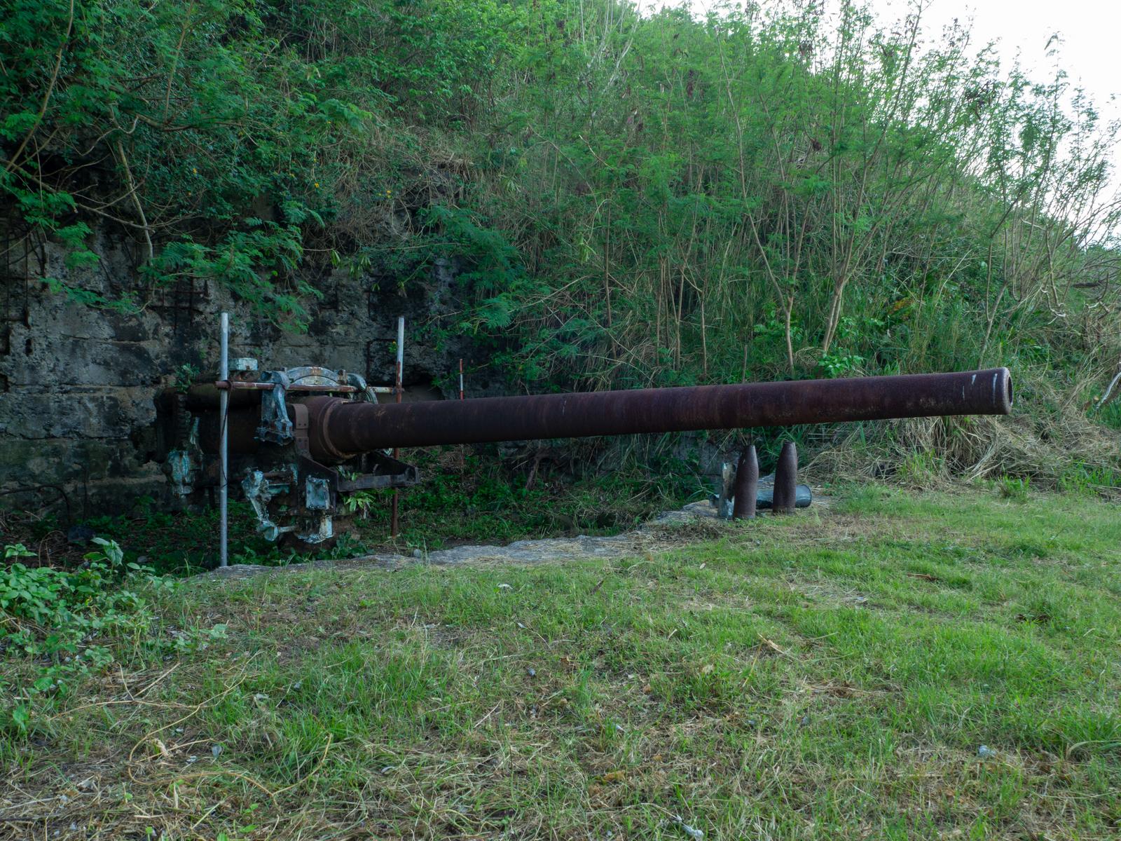 Rusted 14cm naval gun and stone structures - war relics on the grassland