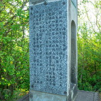 新緑の森林に立つ灰色の石製戦跡慰霊碑の写真