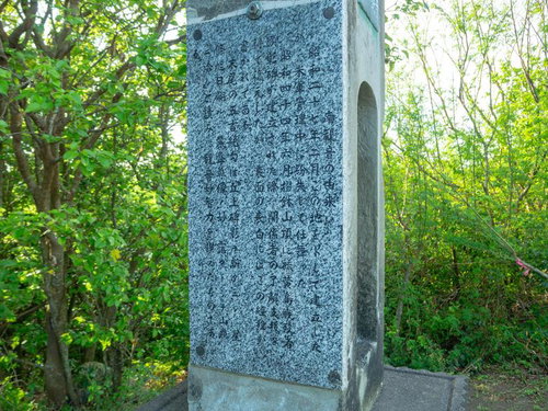 新緑の森林に立つ灰色の石製戦跡慰霊碑