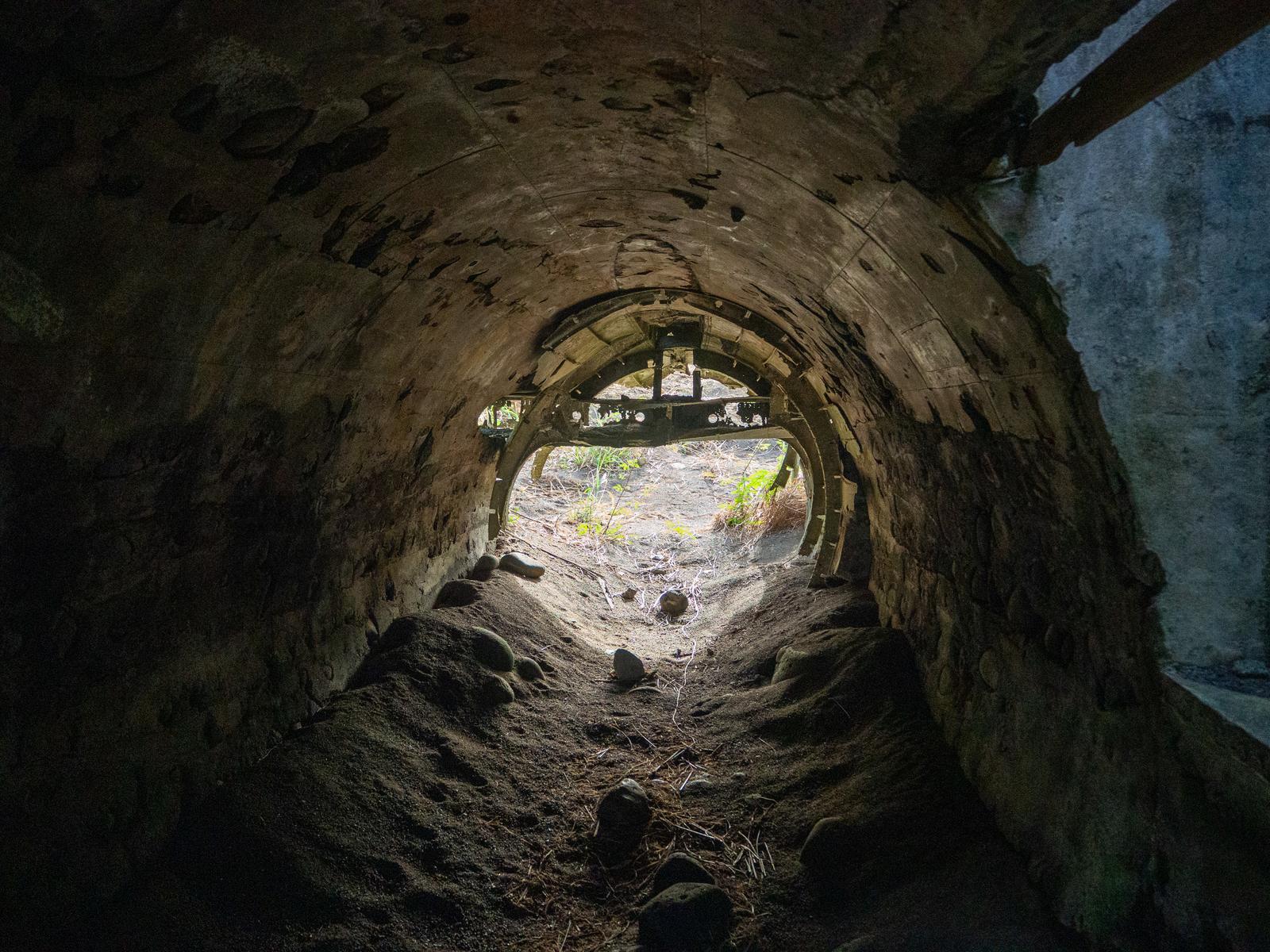 石造りのアーチ型トンネル内部から明るい出口を見た構図