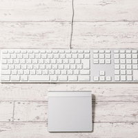 木目調デスクに置かれた白いキーボードとトラックパッドの写真