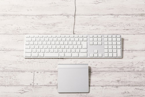 木目調デスクに置かれた白いキーボードとトラックパッド