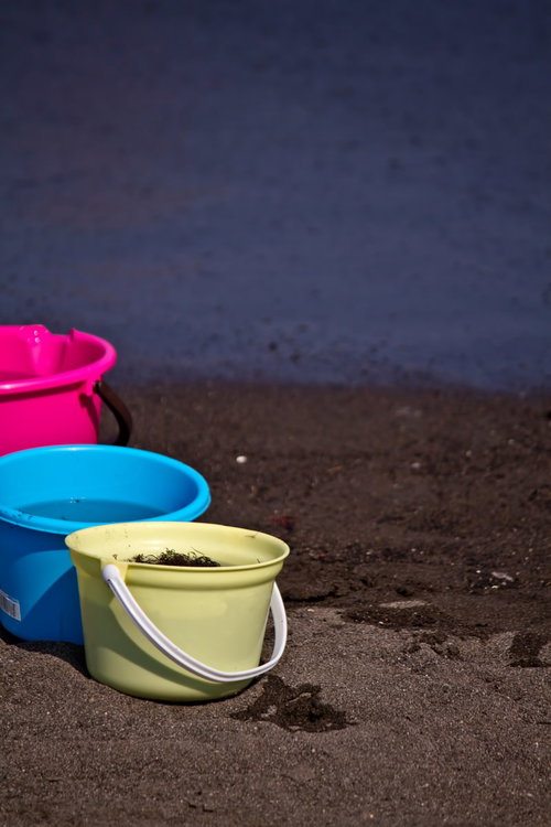 砂浜の水際に並ぶピンク・青・黄緑のカラフルなバケツ