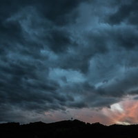 右側にオレンジと白の光が見える暗い雲が覆う嵐の空と山の影の写真