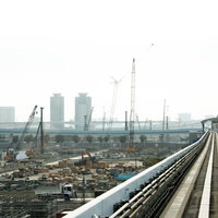 高架の鉄道線路と左側に広がる建設中の工事現場の都市風景の写真