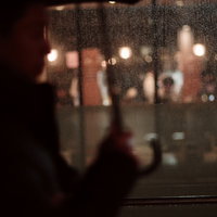 傘をさす通行人が前を通りすぎる雨の夜の写真