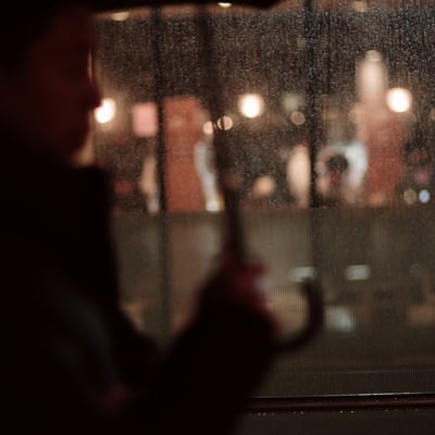 傘をさす通行人が前を通りすぎる雨の夜の写真