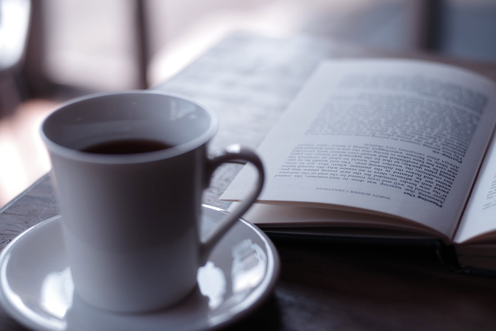 白いソーサーの上のコーヒーカップと開いた洋書が並んでいる