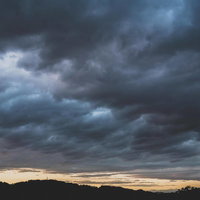 電波塔と山のシルエットが見える暗い雨雲が空を覆う夕暮れの風景の写真