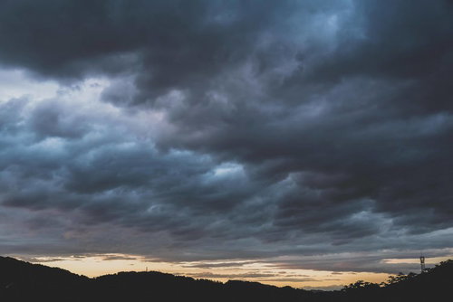 電波塔と山のシルエットが見える暗い雨雲が空を覆う夕暮れの風景