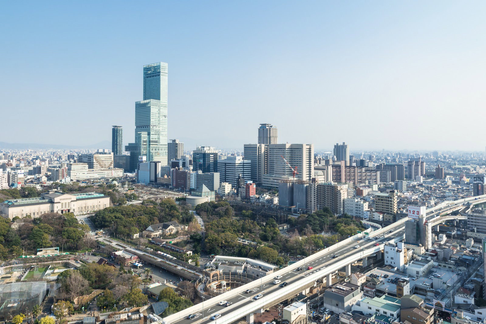 青いガラス張りの超高層ビルと緑の公園がある都市の町並み