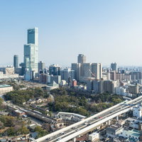 青いガラス張りの超高層ビルと緑の公園がある都市の町並みの写真