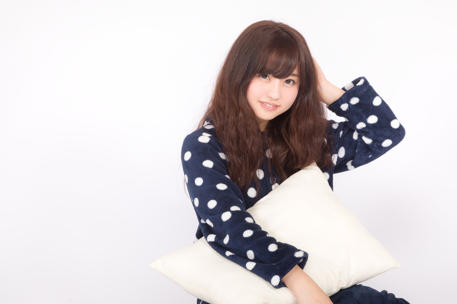 紺色の水玉パジャマを着て白いクッションを抱きながら頭を抱える女性［モデル：河村友歌］
