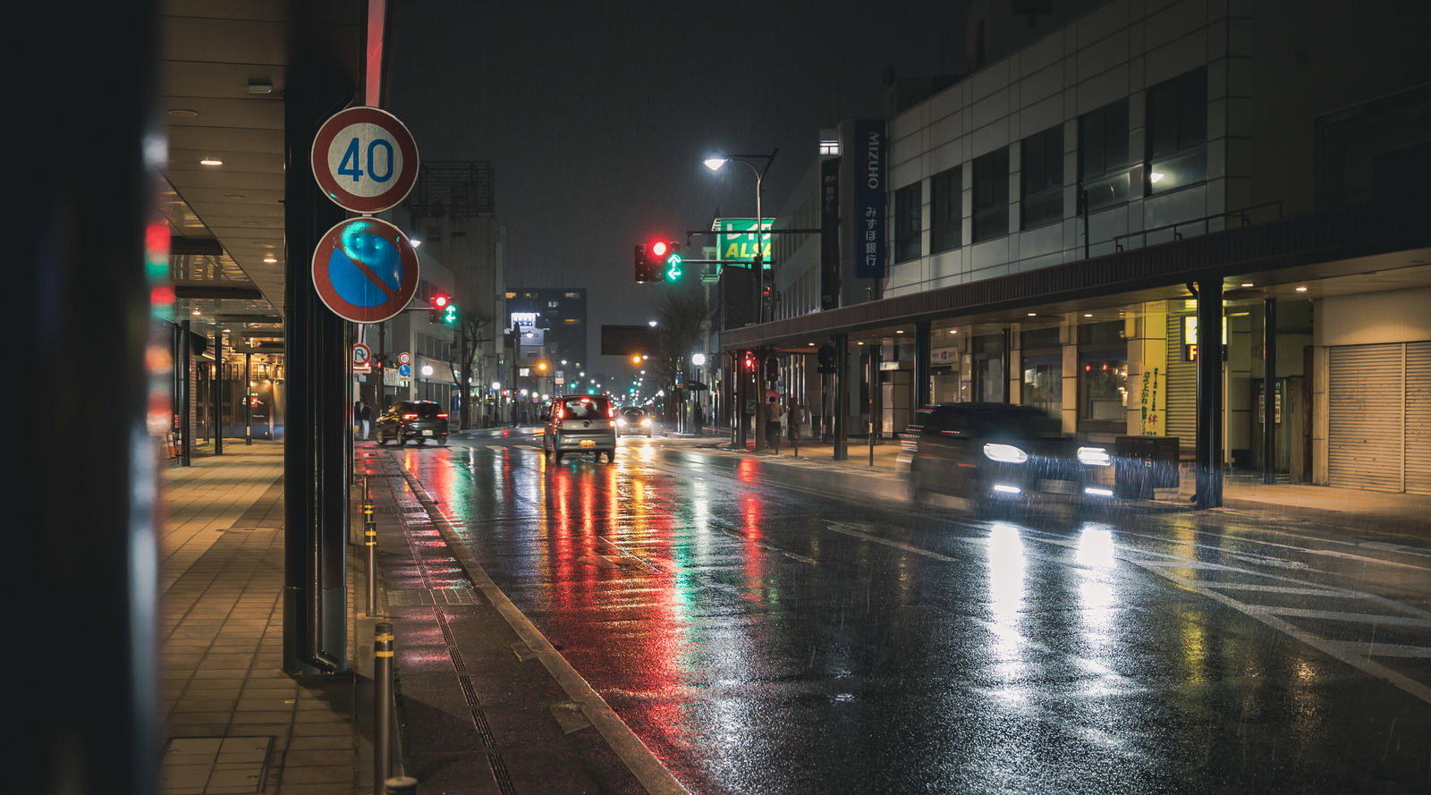 雨の夜間交差点で信号とライトが濡れた路面に反射している風景