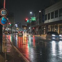 信号と自動車のライトがカラフルに反射する雨の夜間交差点の写真